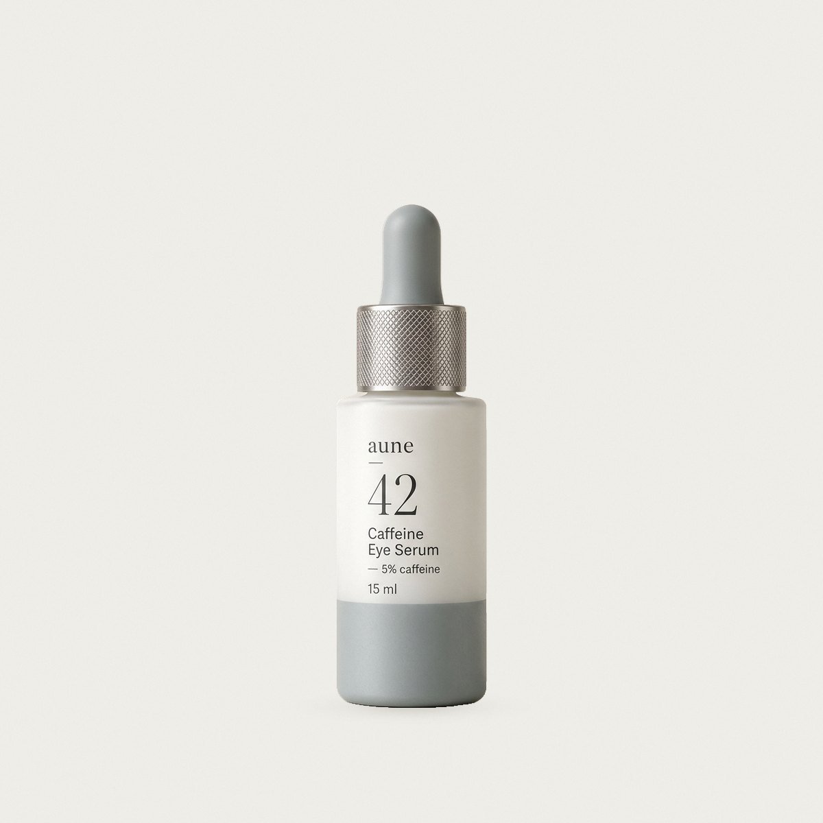 Caffeine Eye Serum in a white glass small dropper bottle with a sea-grey tide line, on a warm white backdrop