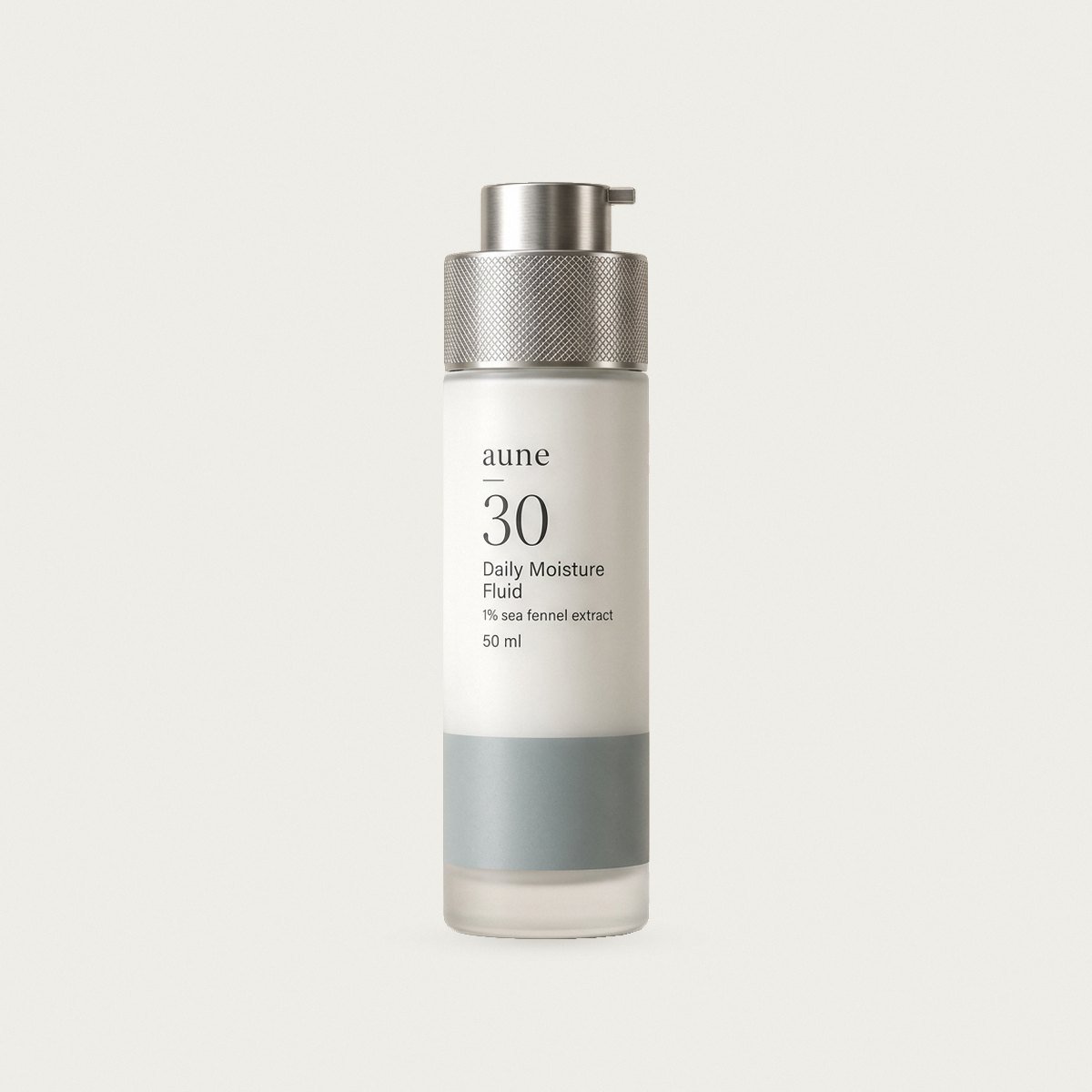 Daily Moisture Fluid in a white glass pump bottle with a sea-grey tide line, on a warm white backdrop