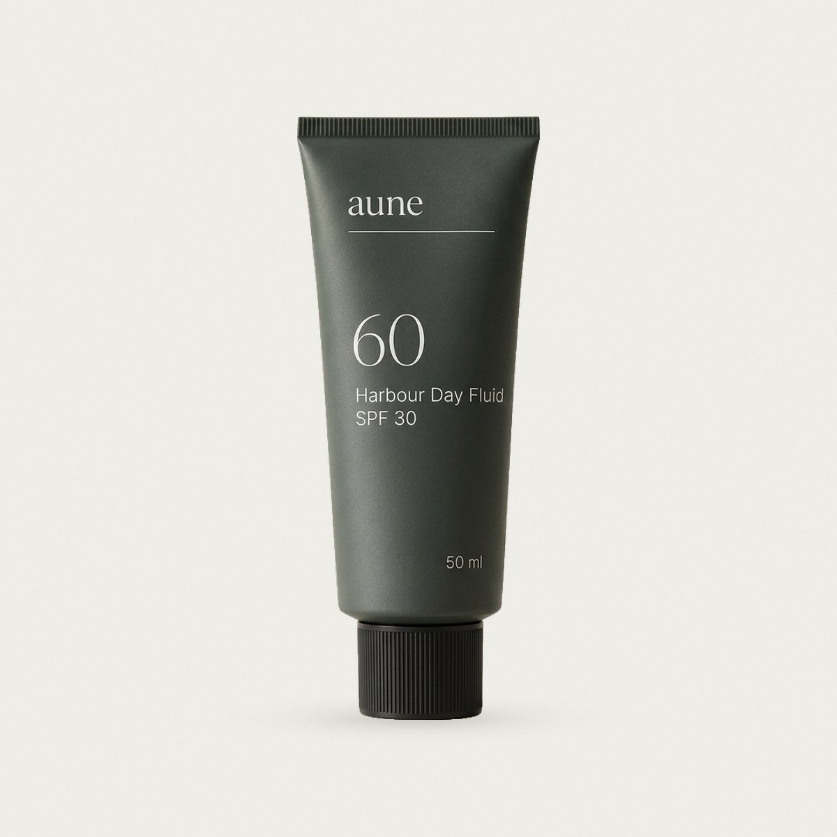 Harbour Day Fluid SPF 30 in a smoked glass tube, on a warm white backdrop