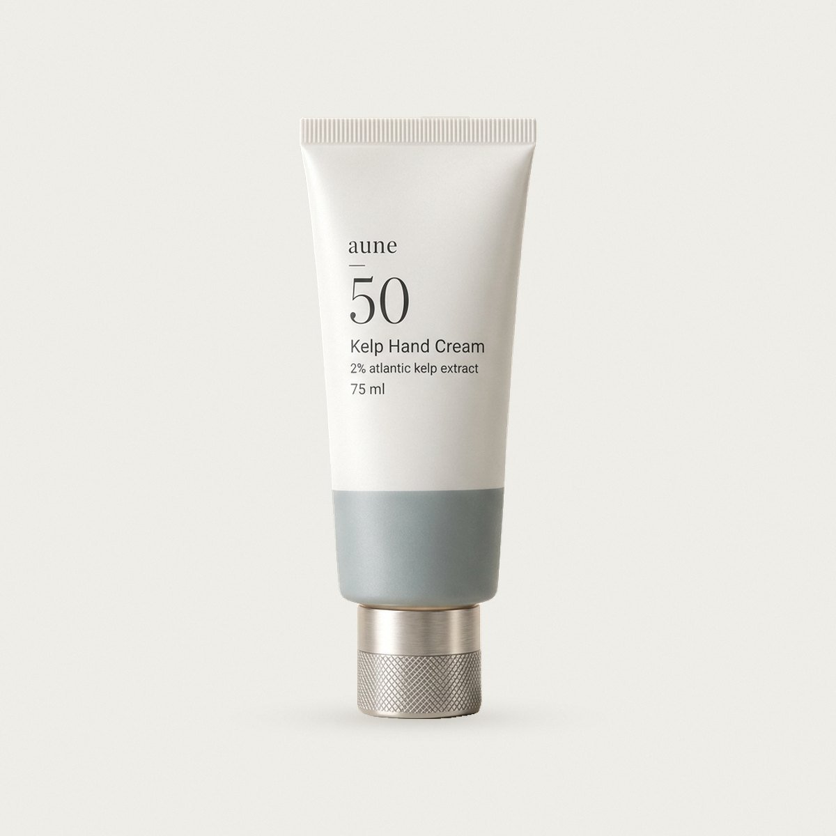 Kelp Hand Cream in a white glass tube with a sea-grey tide line, on a warm white backdrop