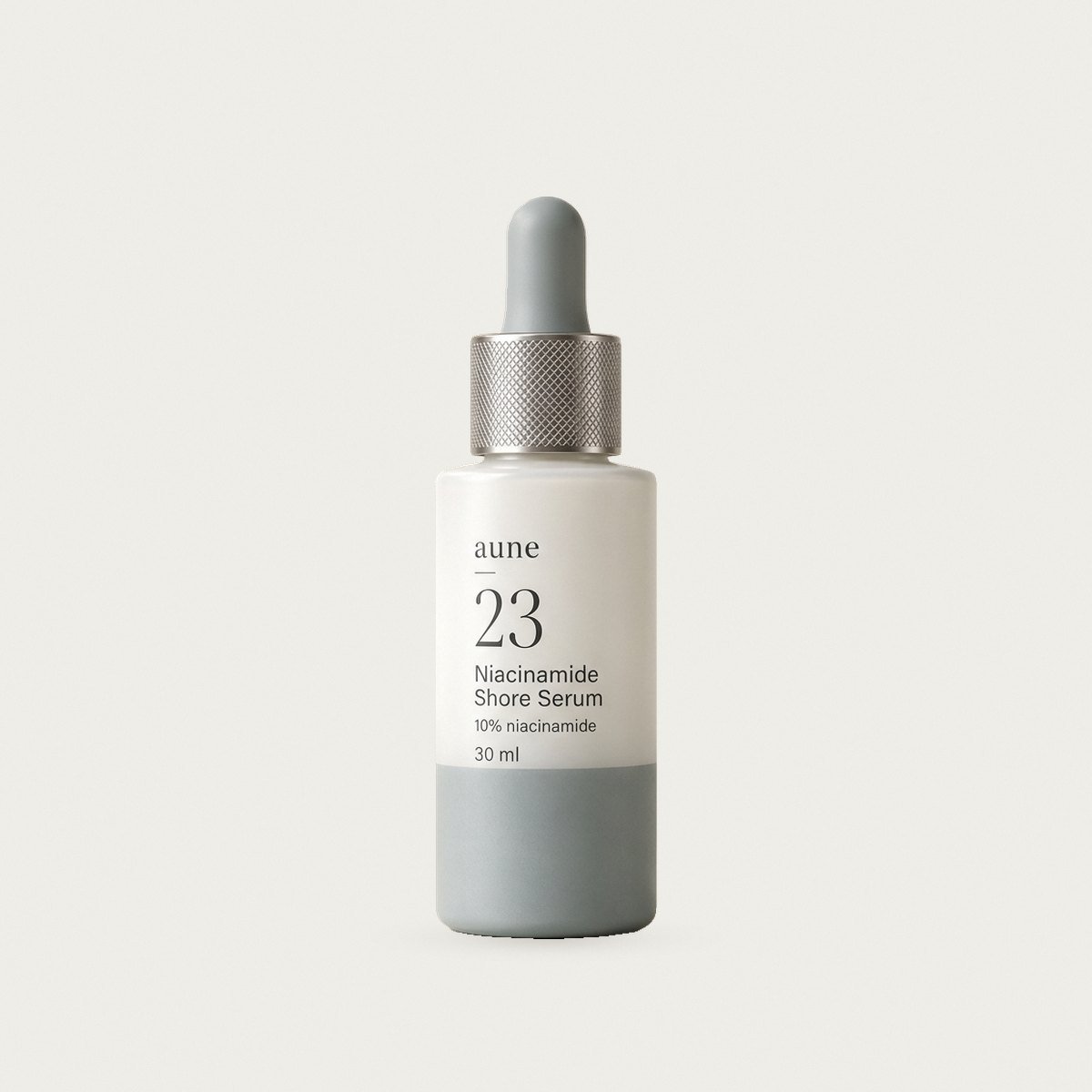 Niacinamide Shore Serum in a white glass dropper bottle with a sea-grey tide line, on a warm white backdrop