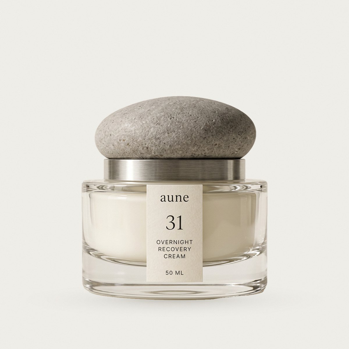 Overnight Recovery Cream in a clear glass cream jar with a stone pebble cap, on a warm white backdrop