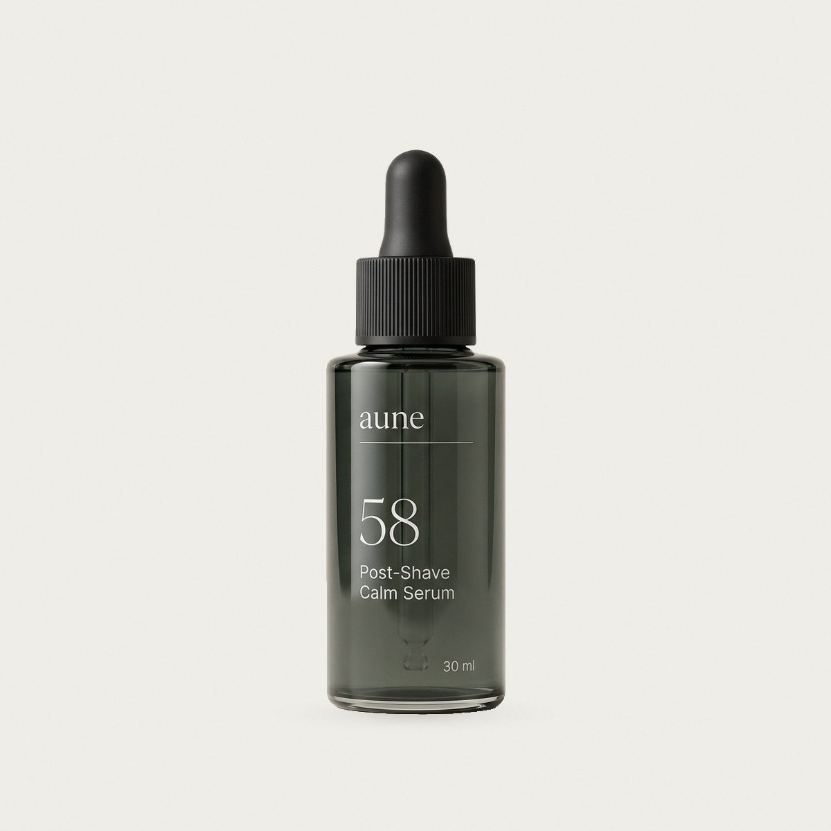 Post-Shave Calm Serum in a smoked glass dropper bottle, on a warm white backdrop