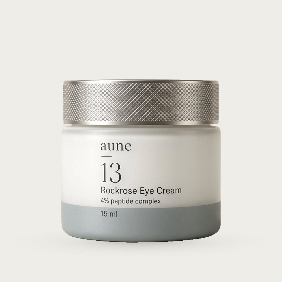 Rockrose Eye Cream in a white glass small jar with a sea-grey tide line, on a warm white backdrop