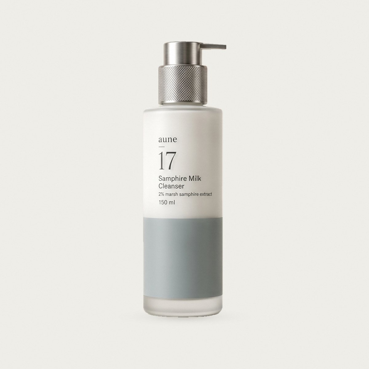Samphire Milk Cleanser in a white glass pump bottle with a sea-grey tide line, on a warm white backdrop