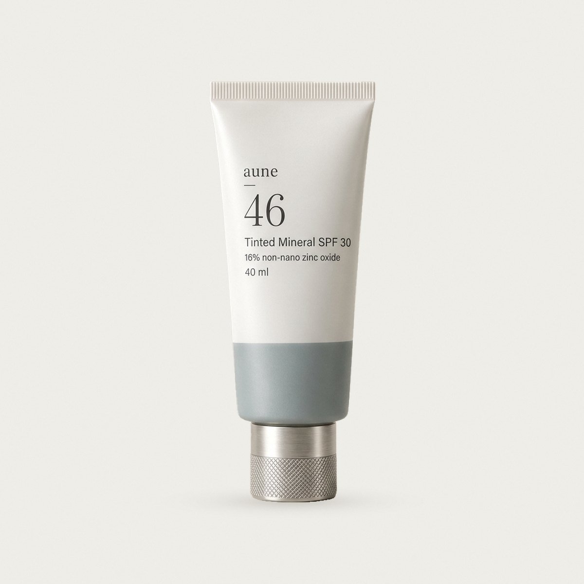 Tinted Mineral SPF 30 in a white glass tube with a sea-grey tide line, on a warm white backdrop